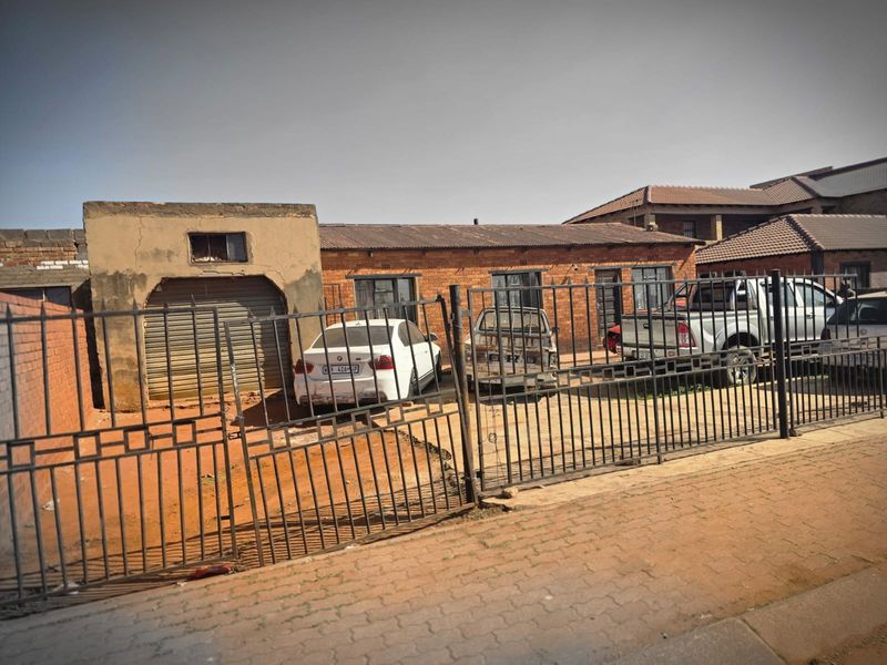 Front view of a single-story brick house featuring a metal security gate, roller shutter garage, and tiled roof.