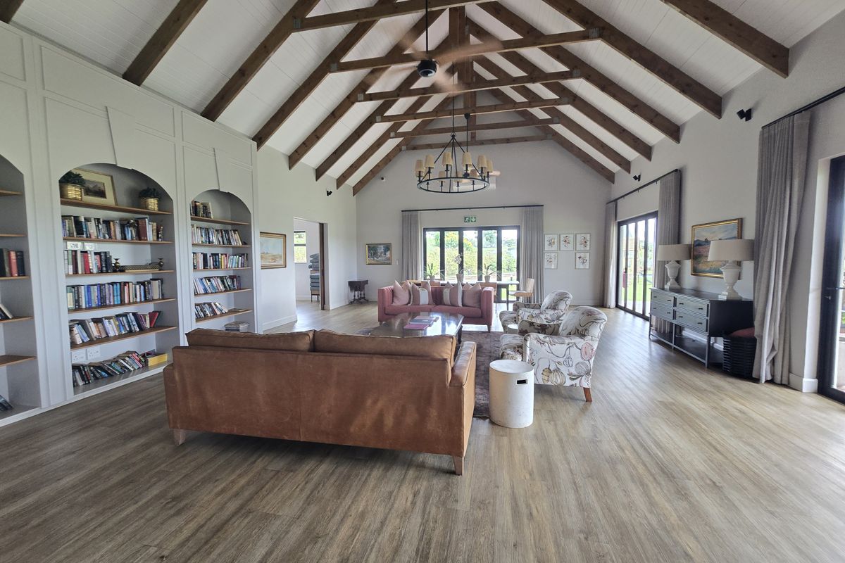 Spacious living room featuring a dramatic vaulted ceiling with exposed timber trusses, built-in shelving, and large glass doors providing ample natural light.