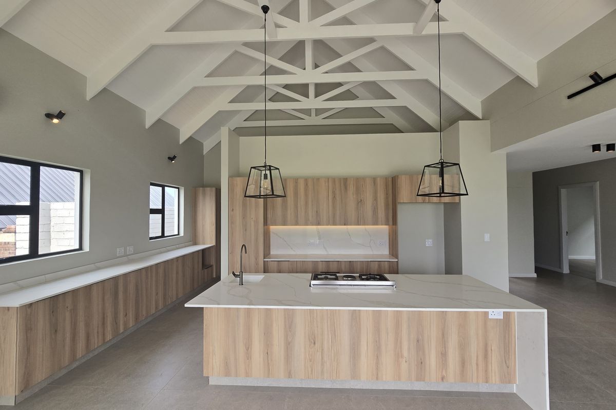 Modern kitchen featuring a high vaulted ceiling with exposed trusses, a central island with stone countertops, gas cooktop, and sleek wood-finish cabinetry.