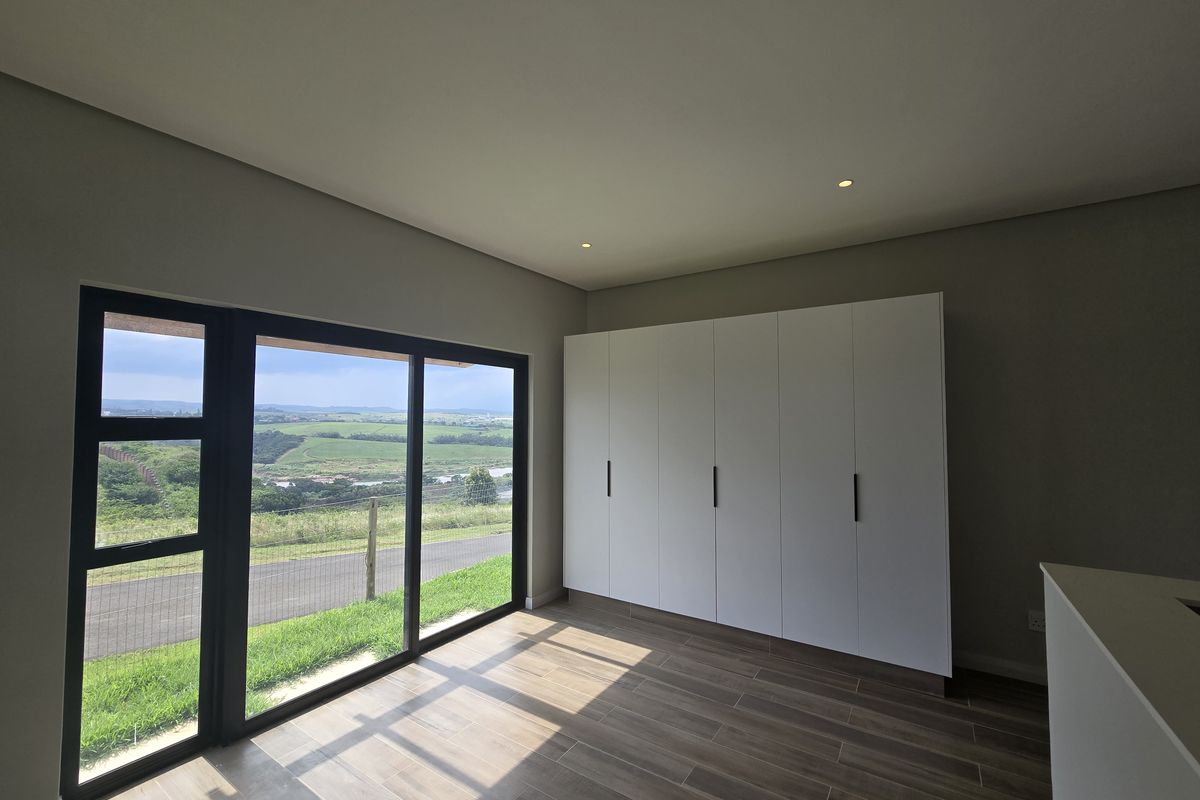 A bright, modern bedroom featuring sleek built-in cupboards, tiled flooring, and large sliding glass doors that offer expansive views of the surrounding landscape.