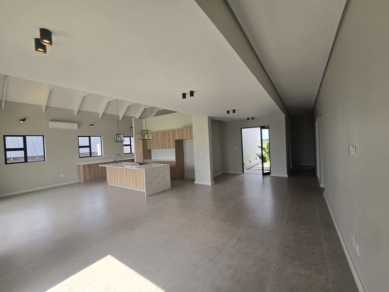 Spacious open-plan living and kitchen area featuring modern cabinetry, a central island with stone countertops, vaulted ceilings, and large tiled floors.