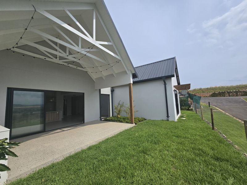 A modern covered patio area featuring exposed white timber trusses, concrete flooring, and large sliding glass doors leading into the main living space.