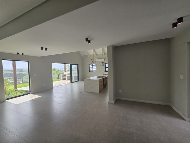 Spacious open-plan living and kitchen area featuring a modern island, vaulted ceilings, large format tiling, and seamless access to an outdoor patio with views.