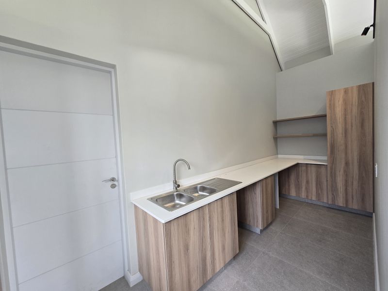 A modern, clean scullery featuring wood-look cabinetry, stone countertops, a double sink, and high vaulted ceilings, providing ample storage and workspace.