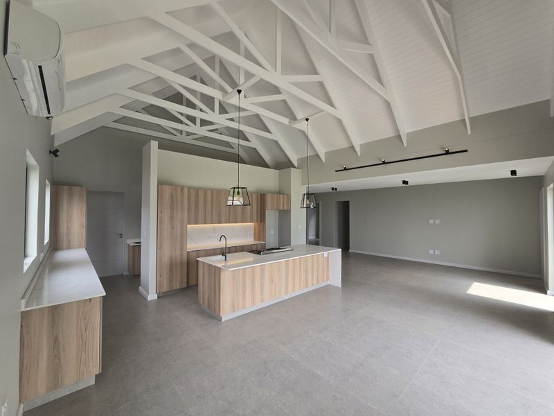 Spacious open-plan living area featuring a modern kitchen with wood-finish cabinetry, stone countertops, a central island, and a striking vaulted ceiling with exposed trusses.