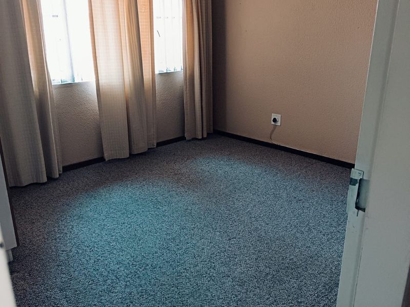 An empty bedroom featuring carpeted flooring, a ceiling fan, and window security bars, offering a blank canvas for personalization.