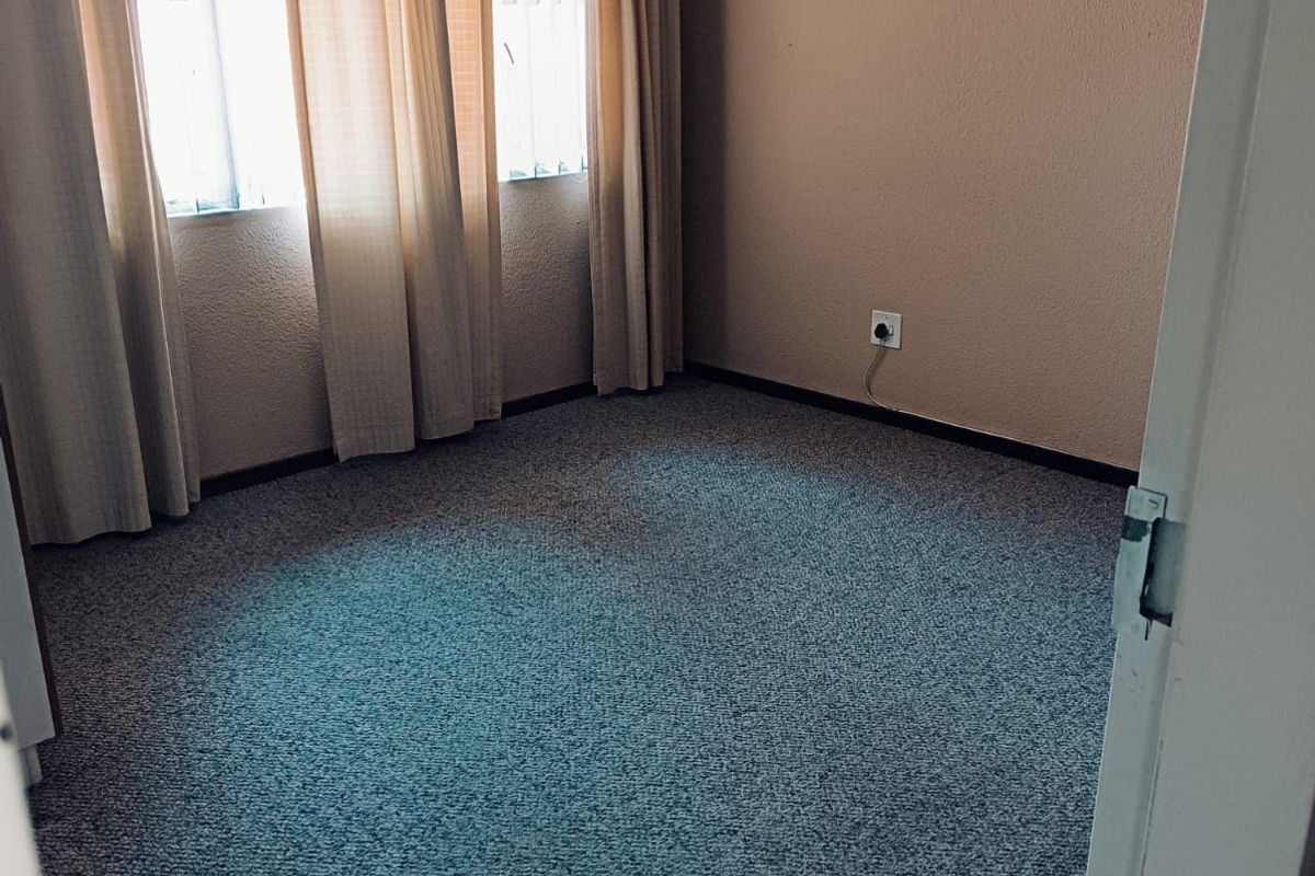 An empty bedroom featuring carpeted flooring, a ceiling fan, and window security bars, offering a blank canvas for personalization.