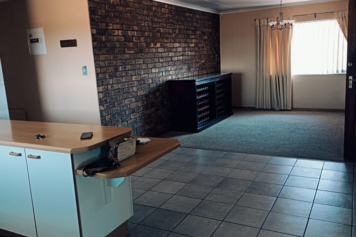 Open plan living area featuring a prominent exposed brick wall, tiled flooring, and a functional kitchen island, offering a versatile space for modern living.