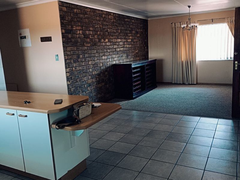 Open plan living area featuring a prominent exposed brick wall, tiled flooring, and a functional kitchen island, offering a versatile space for modern living.