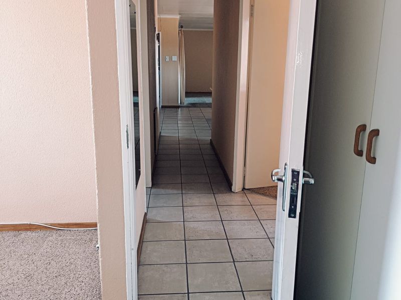 A view through a doorway into a tiled hallway connecting to other rooms, featuring built-in storage and neutral wall finishes.