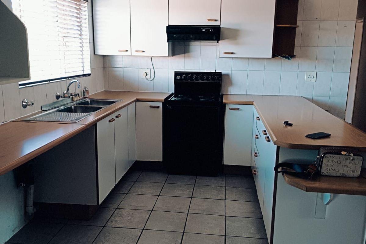 A functional kitchen featuring white cabinetry, laminate countertops, a stainless steel sink, and a freestanding stove with an extractor fan.