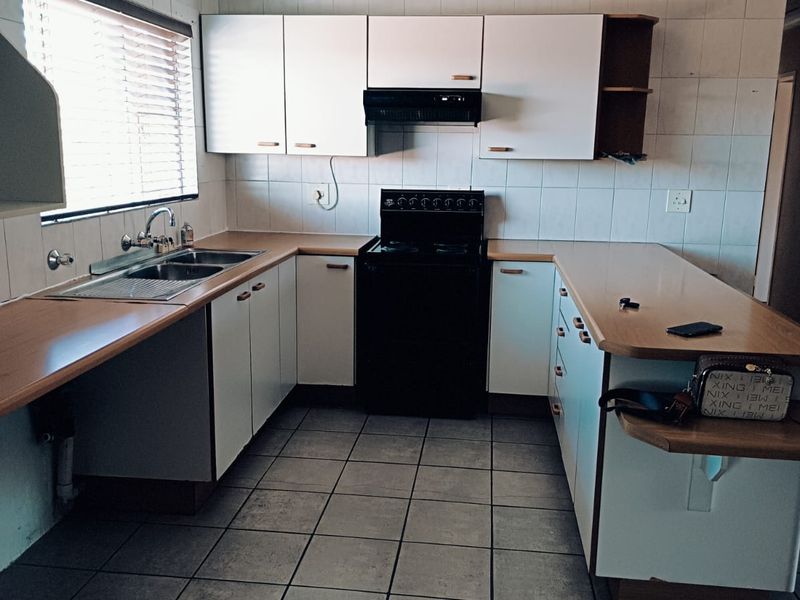 A functional kitchen featuring white cabinetry, laminate countertops, a stainless steel sink, and a freestanding stove with an extractor fan.