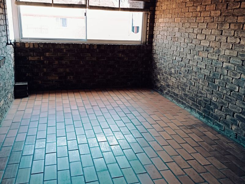 An empty covered patio area featuring exposed brick walls, tiled flooring, and a corrugated metal roof, offering a blank canvas for outdoor living.