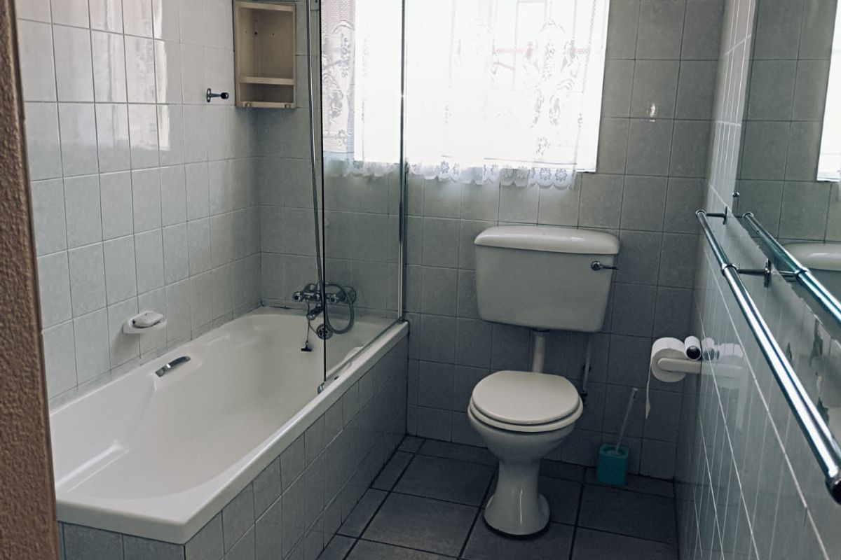 A functional bathroom featuring a bathtub with a glass screen, a toilet, and full-height wall tiling.
