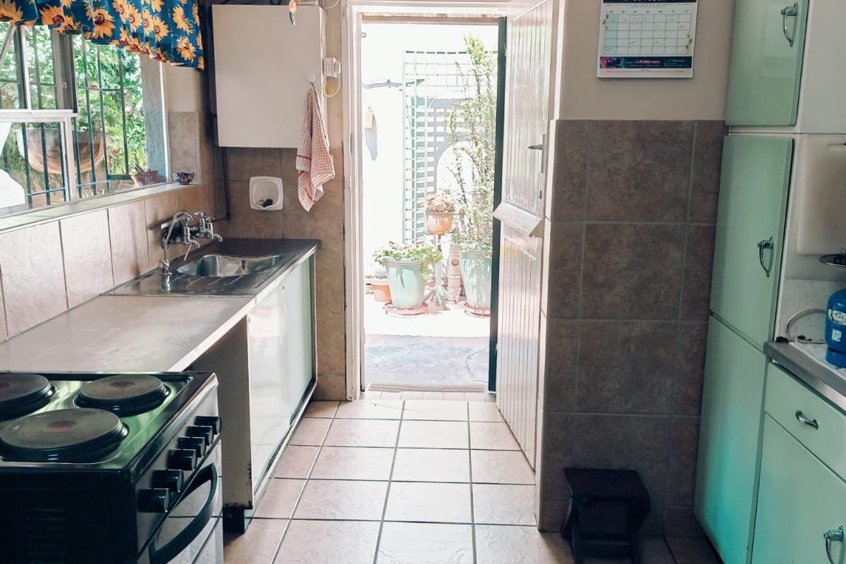 A functional kitchen featuring tiled flooring, built-in cabinetry, a stainless steel sink, and an electric stove, with direct access to an outdoor area.