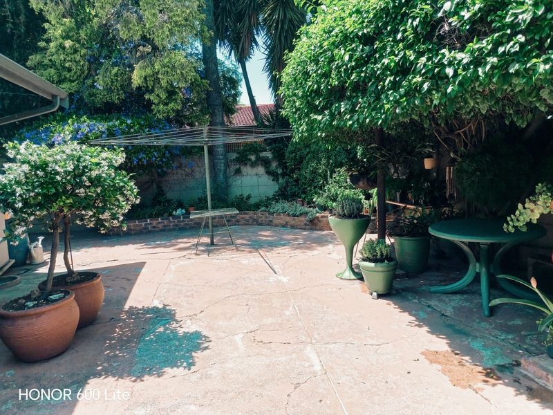 A private garden area featuring a paved patio, brick retaining wall, and established trees, providing a quiet outdoor space.