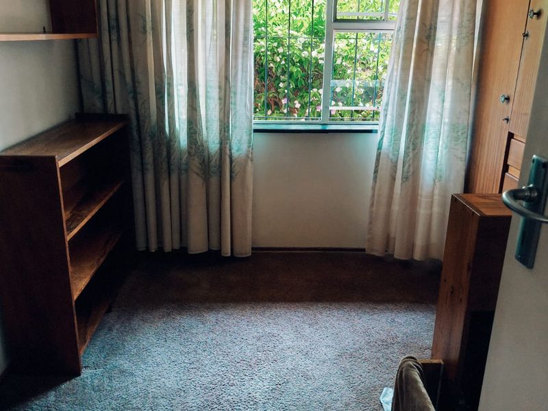 A bedroom featuring built-in wooden shelving and a wardrobe, with carpeted flooring and a window fitted with security bars.
