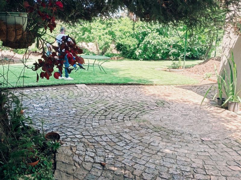 A private garden area featuring a circular cobblestone patio, well-maintained lawn, and mature trees providing shade.