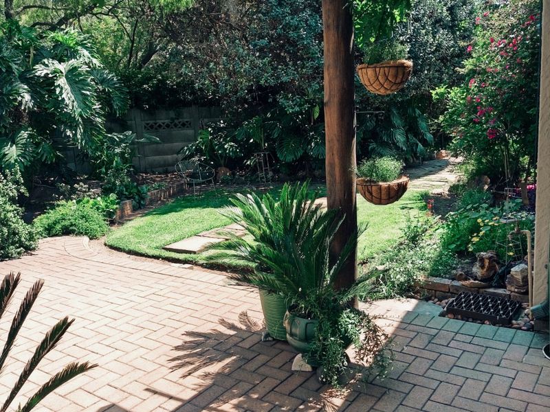 A charming outdoor patio area featuring a timber pergola structure and brick paving, overlooking a lush, well-established garden.