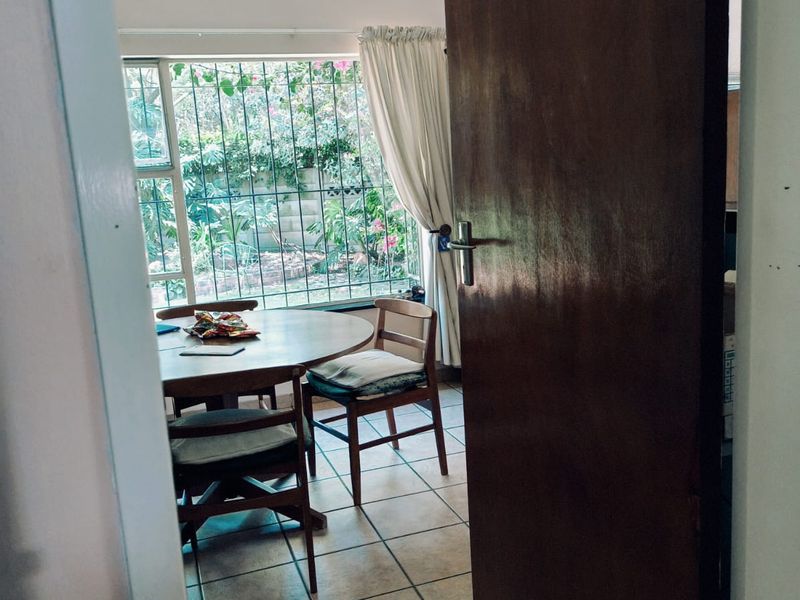 A dining area featuring tiled flooring, track lighting, and large windows with security bars overlooking the garden.