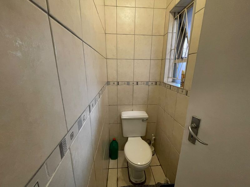 A compact guest toilet featuring full-height ceramic wall tiling, tiled flooring, and a window with a security gate.
