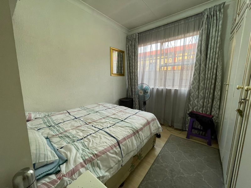 A functional bedroom featuring built-in cupboards, coving, and a window fitted with security bars.