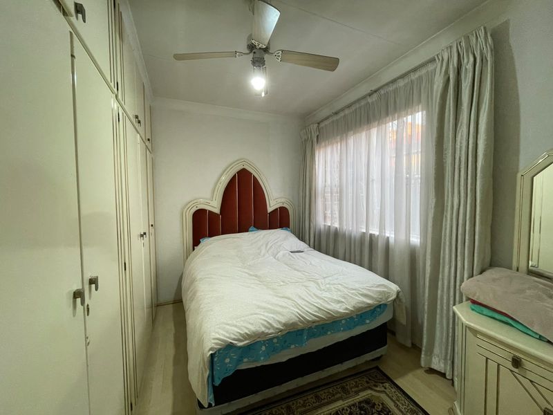 A functional bedroom featuring extensive built-in cupboard storage, a ceiling fan, and laminate flooring, offering a practical layout for comfortable living.