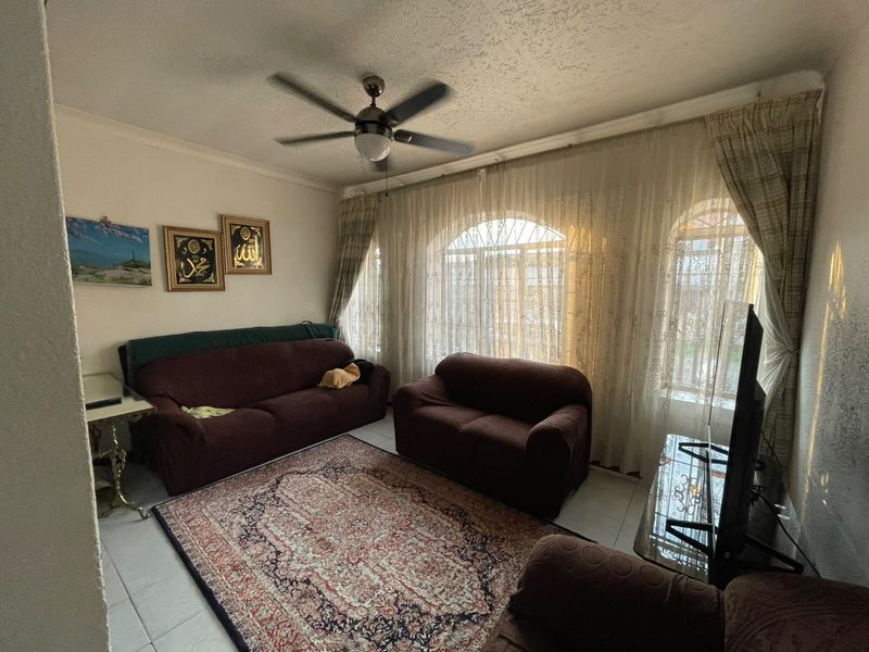 A comfortable living room featuring tiled flooring, a ceiling fan, and large arched windows with natural light.