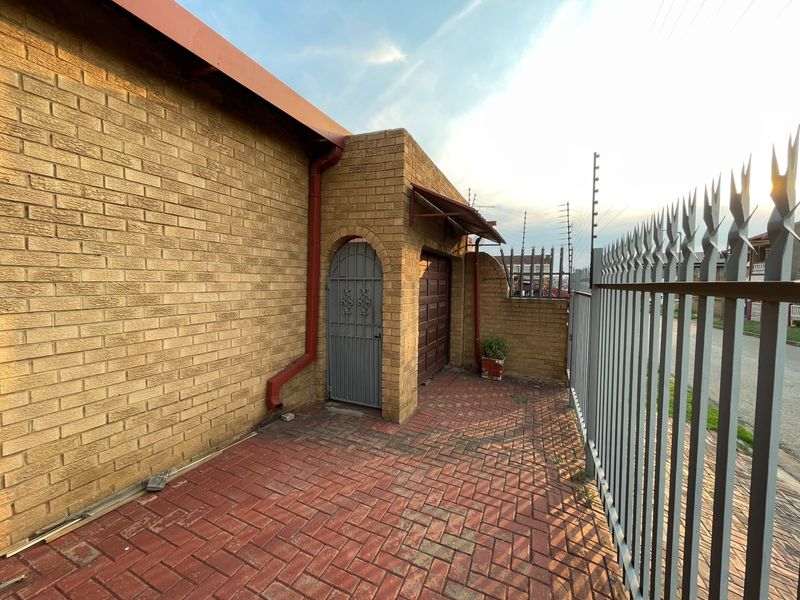 Exterior view of the property featuring a face brick facade, paved driveway, secure steel palisade fencing, and electric security measures.