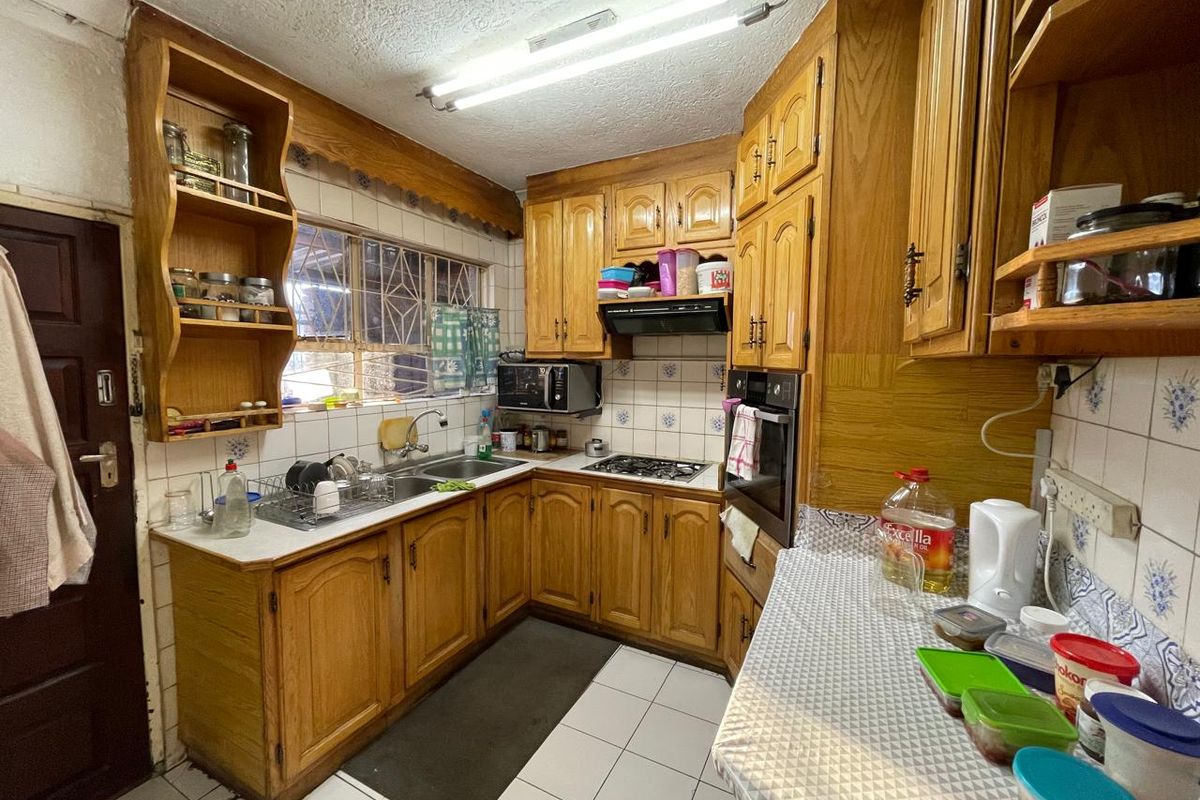 A functional kitchen featuring traditional wooden cabinetry, a double basin sink, built-in oven, and gas hob with tiled backsplash and flooring.