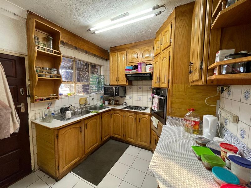 A functional kitchen featuring traditional wooden cabinetry, a double basin sink, built-in oven, and gas hob with tiled backsplash and flooring.