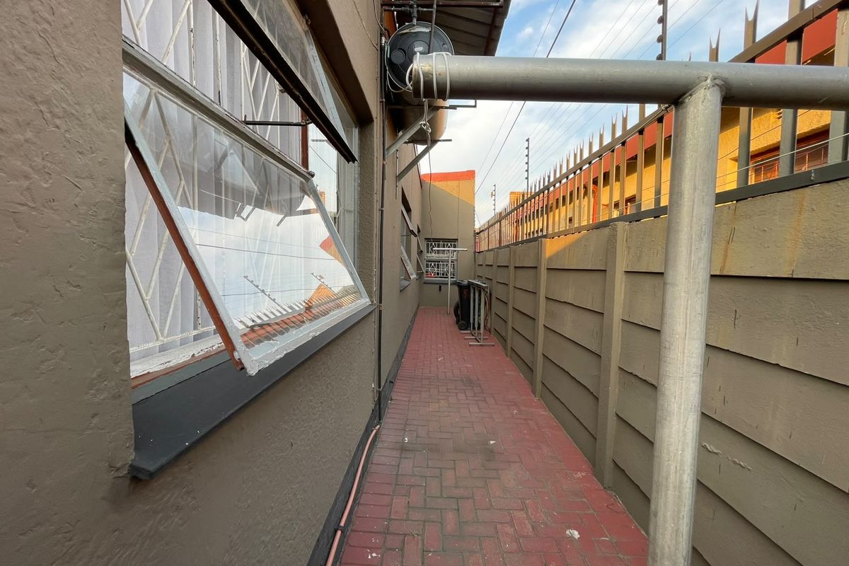 A narrow paved side passage featuring a precast boundary wall with electric fencing and security bars on the windows.