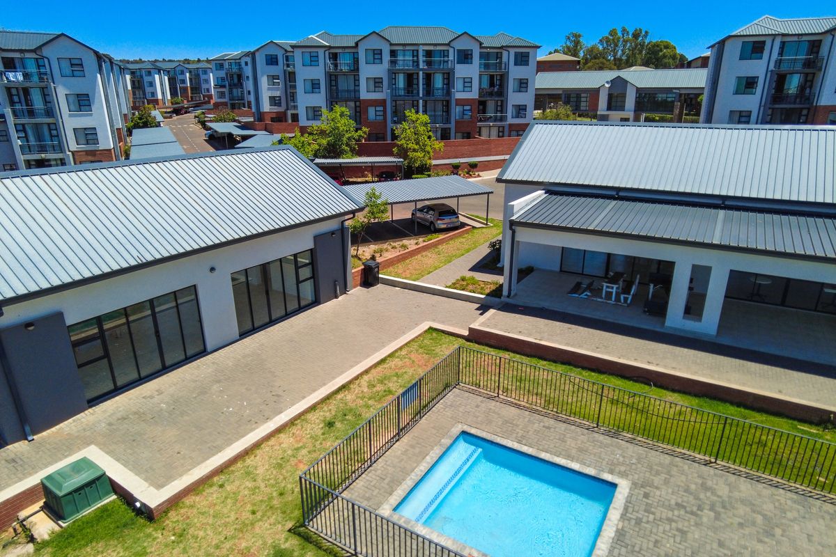 Aerial view of an apartment complex featuring a swimming pool, paved communal areas, and covered parking facilities.