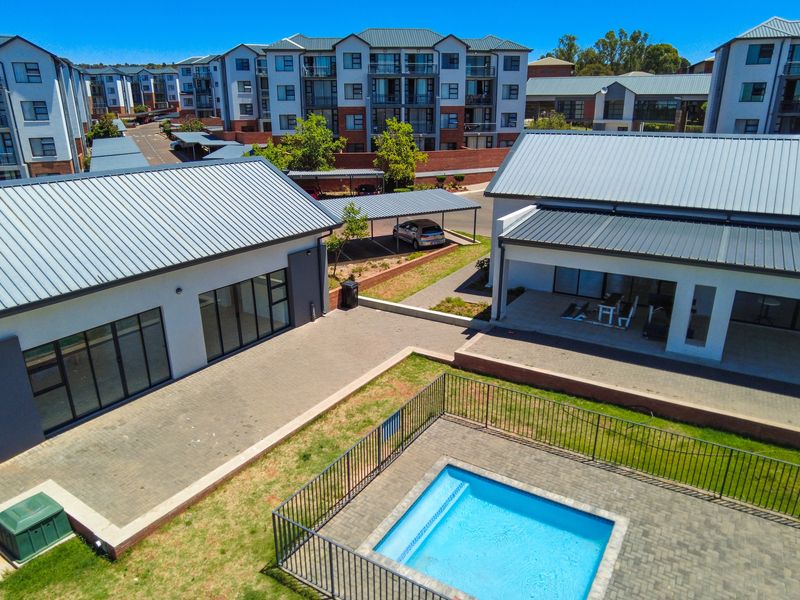 Aerial view of an apartment complex featuring a swimming pool, paved communal areas, and covered parking facilities.