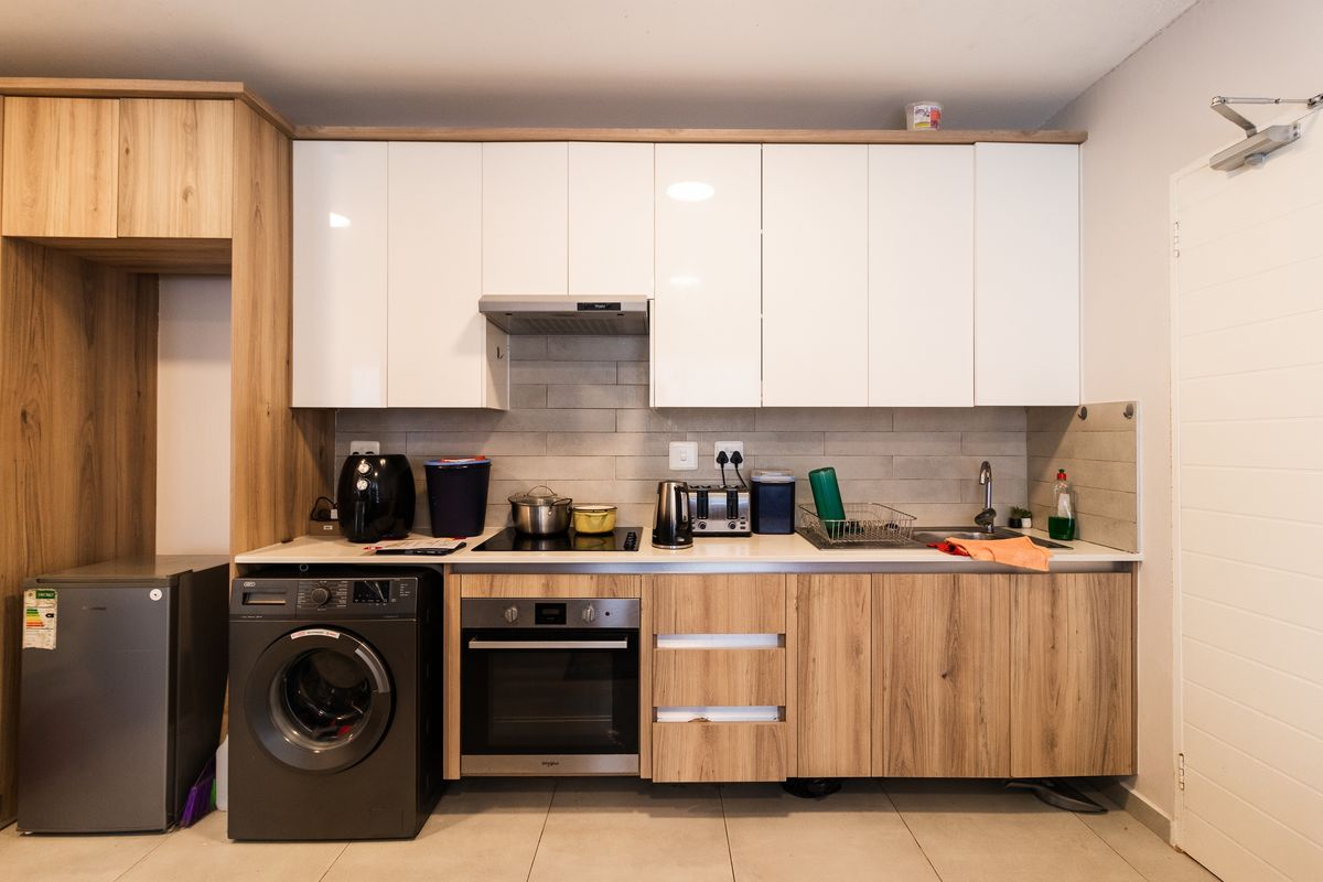 Modern kitchen featuring white and wood-grain cabinetry, built-in oven, electric hob, extractor fan, and tiled backsplash with integrated laundry appliance space.
