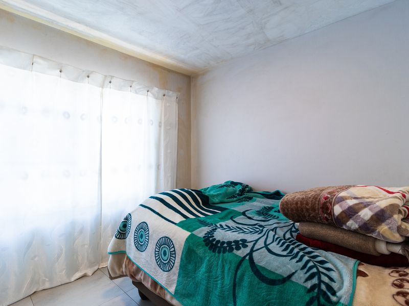 A bedroom featuring tiled flooring, currently showing visible signs of water damage on the ceiling and walls.
