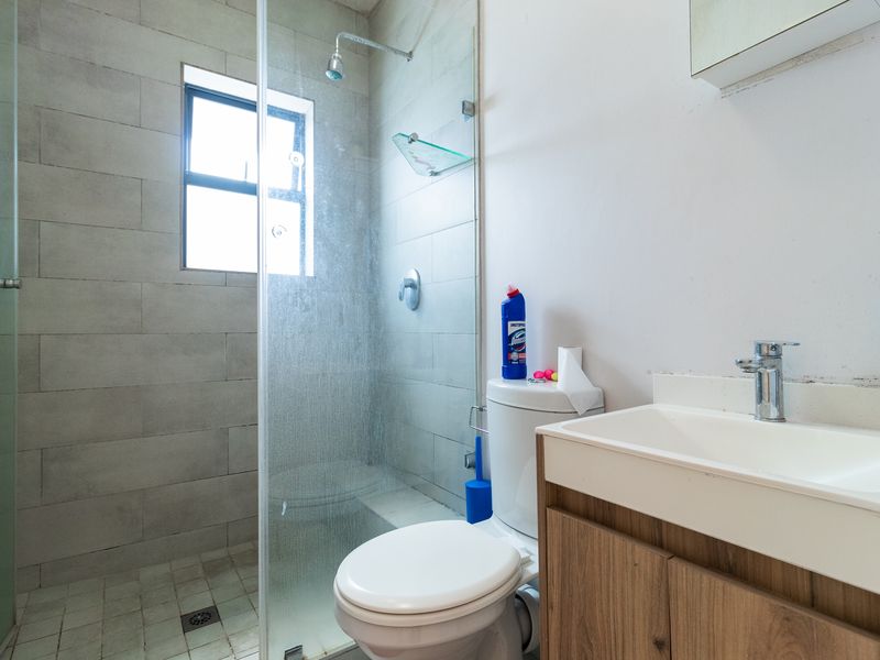 A functional bathroom featuring a glass-enclosed shower, a modern vanity with basin, and a standard toilet, finished with neutral wall tiling.