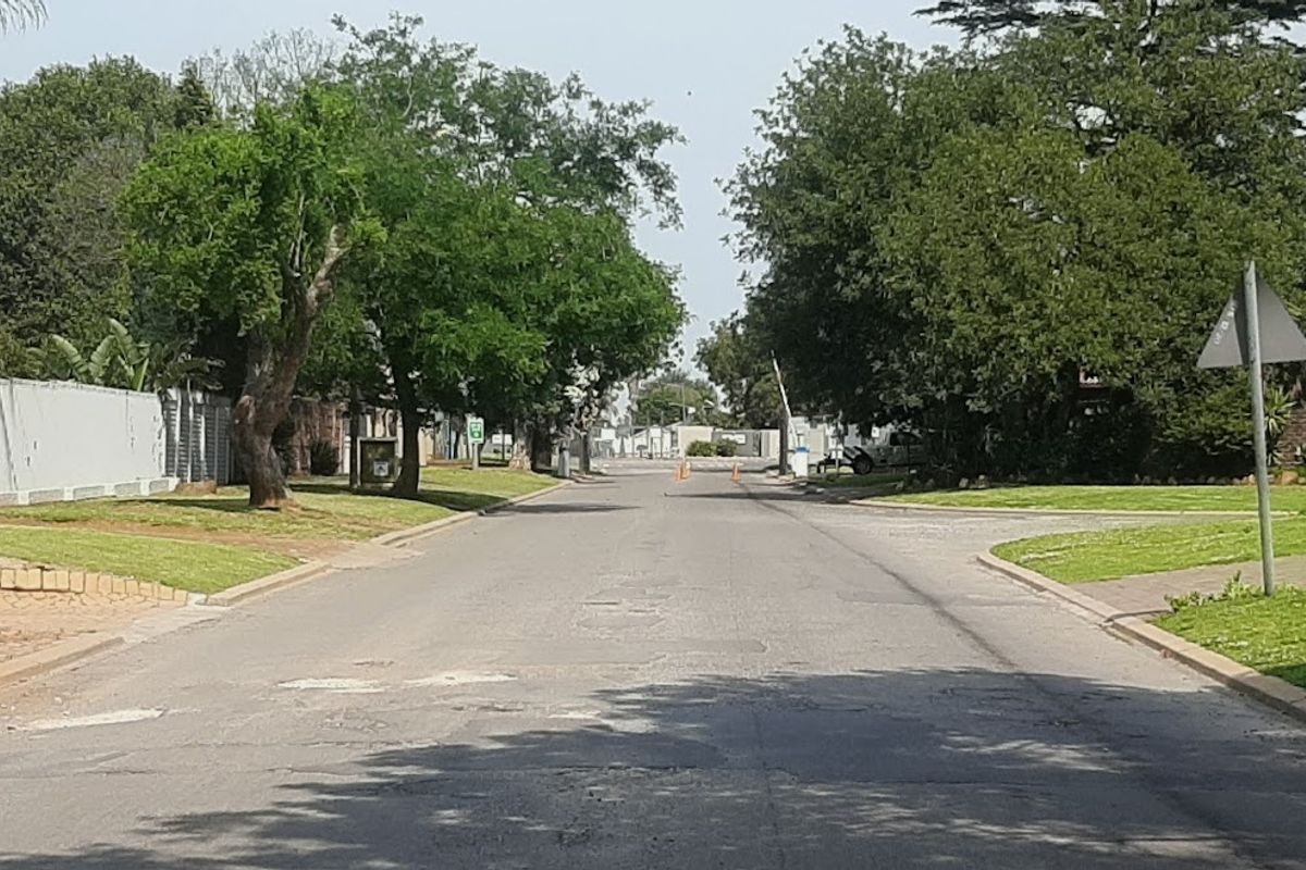 A view of a quiet residential street lined with mature trees, featuring paved sidewalks and grass verges.