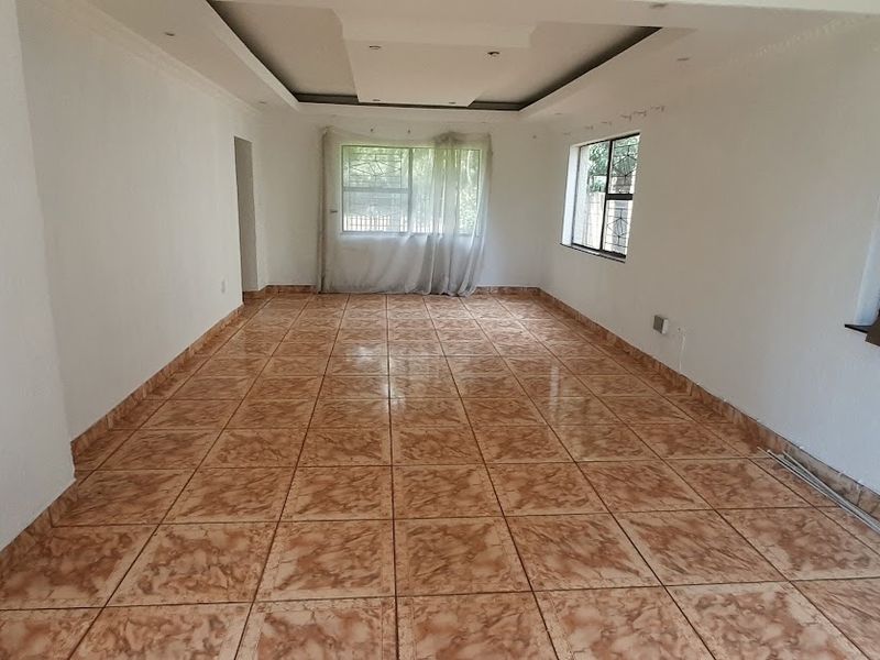 A spacious, empty living area featuring neutral walls, tiled flooring, and a recessed ceiling with integrated lighting, offering a blank canvas for interior design.