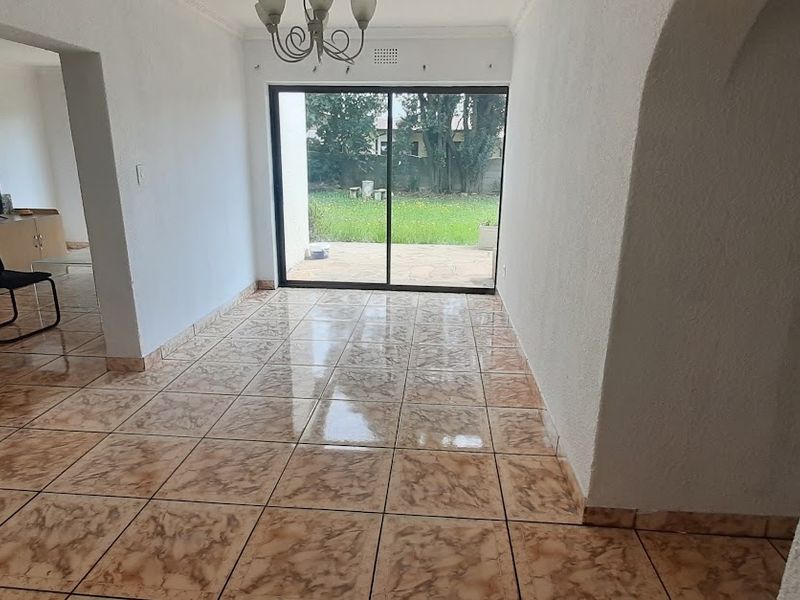 An open-plan living area featuring ceramic floor tiles, an arched entryway, and a sliding glass door providing direct access to the rear garden.