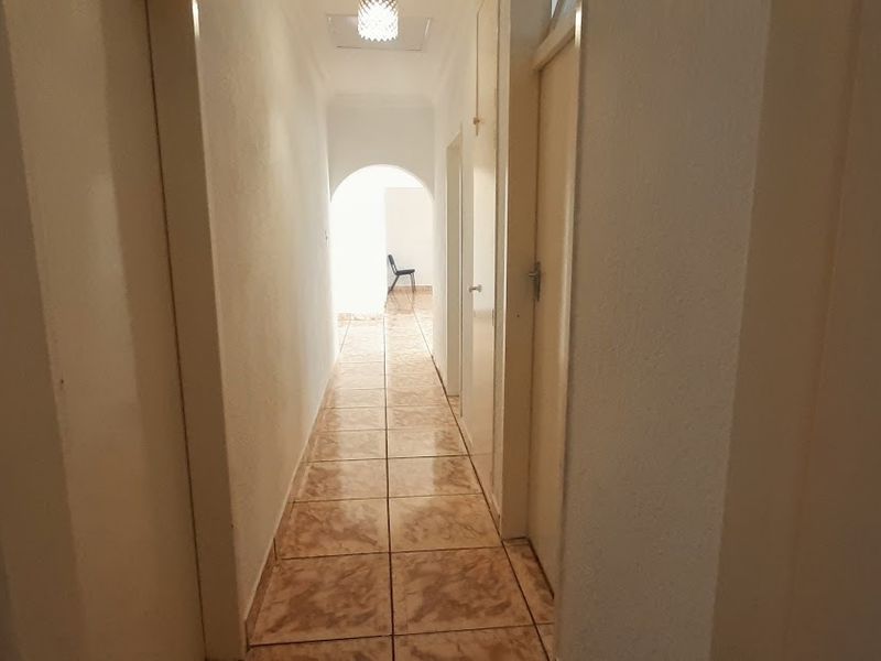 A narrow interior hallway featuring tiled flooring and an arched transition, leading towards an open space at the end.