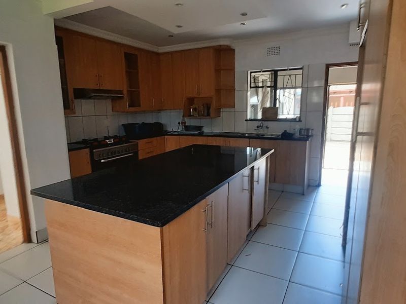 Spacious kitchen featuring a central island with granite countertops, built-in cabinetry, gas hob, and tiled flooring, offering a functional layout for modern living.