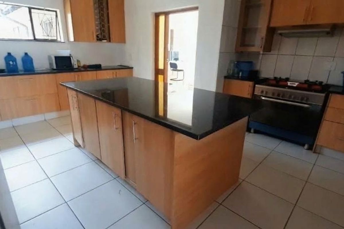 A functional kitchen featuring wooden cabinetry, a central island with a granite countertop, tiled flooring, and a built-in gas stove with an extractor fan.