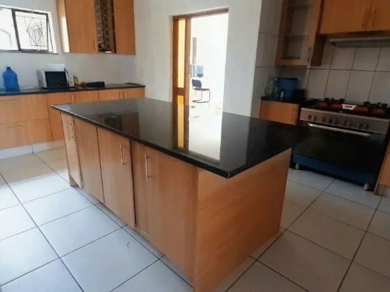 A functional kitchen featuring wooden cabinetry, a central island with a granite countertop, tiled flooring, and a built-in gas stove with an extractor fan.