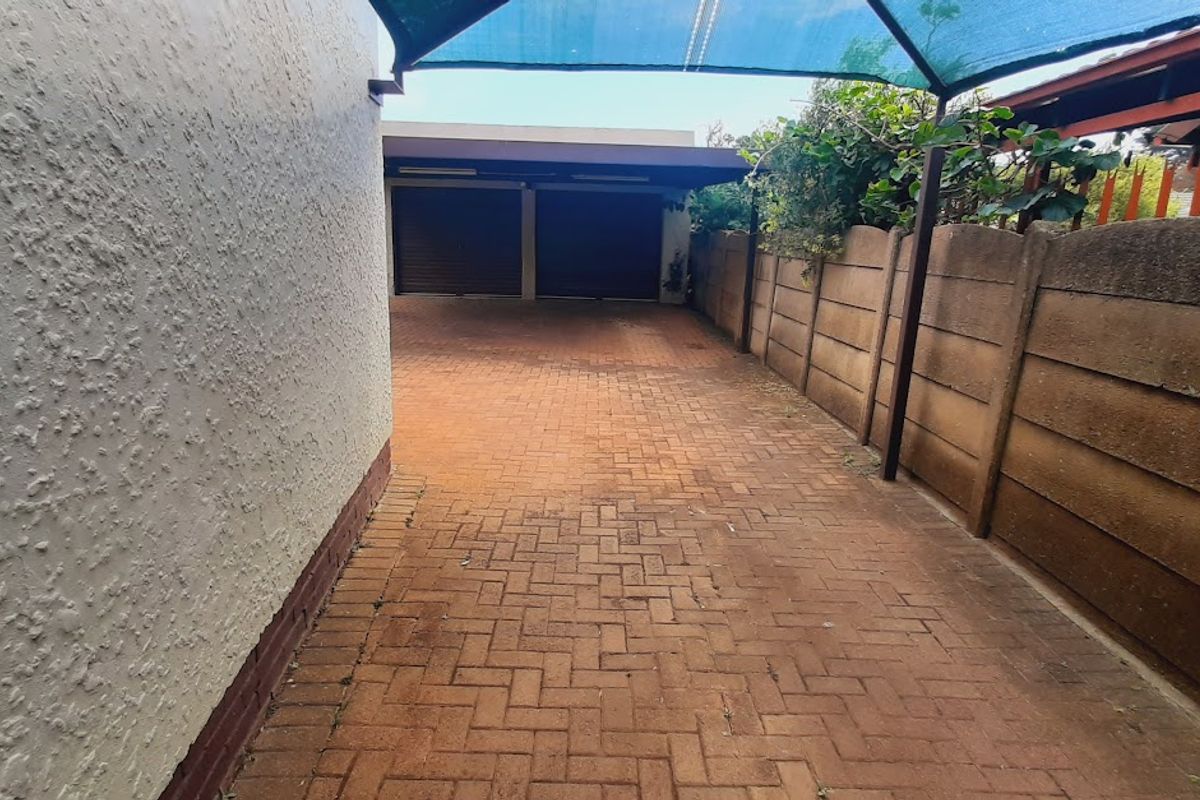 A paved driveway leading to a double garage, enclosed by a precast concrete boundary wall and featuring a shade cloth canopy.