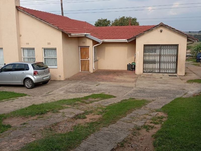 Front elevation of a single-story house featuring a tiled roof, attached garage with security gate, and a paved driveway area.