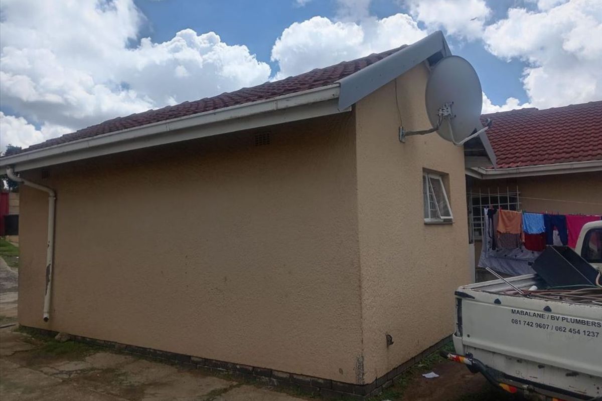 Rear exterior view of the property featuring a tiled roof, plastered walls, and a mounted satellite dish.