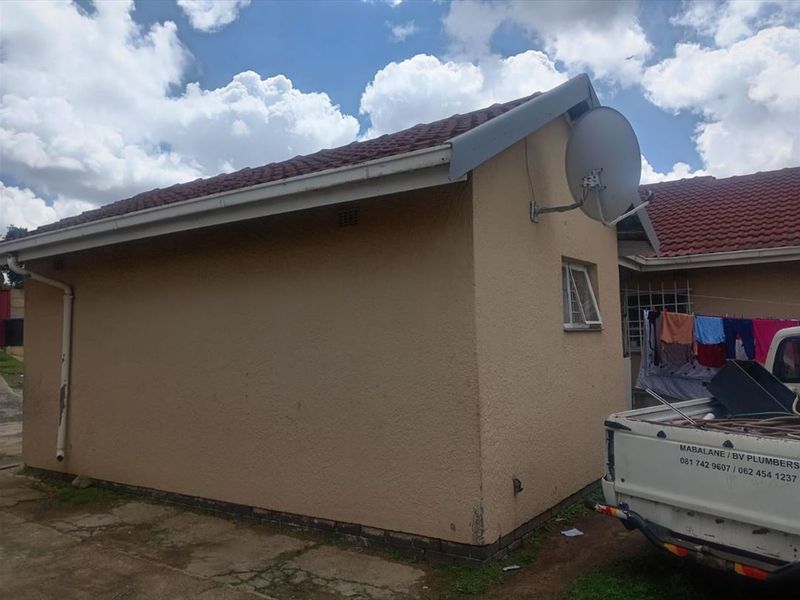 Rear exterior view of the property featuring a tiled roof, plastered walls, and a mounted satellite dish.