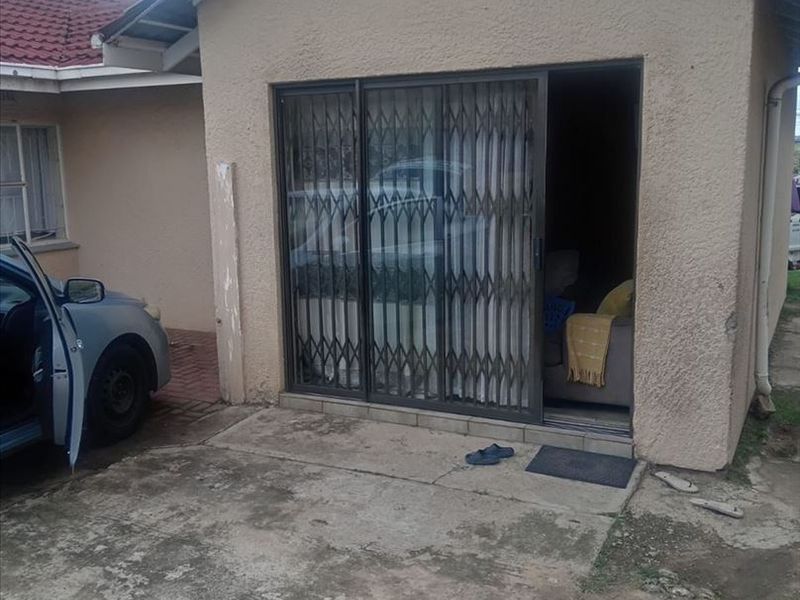 Rear exterior view of the property featuring a concrete patio area, sliding glass door with security gate, and tiled roof structure.