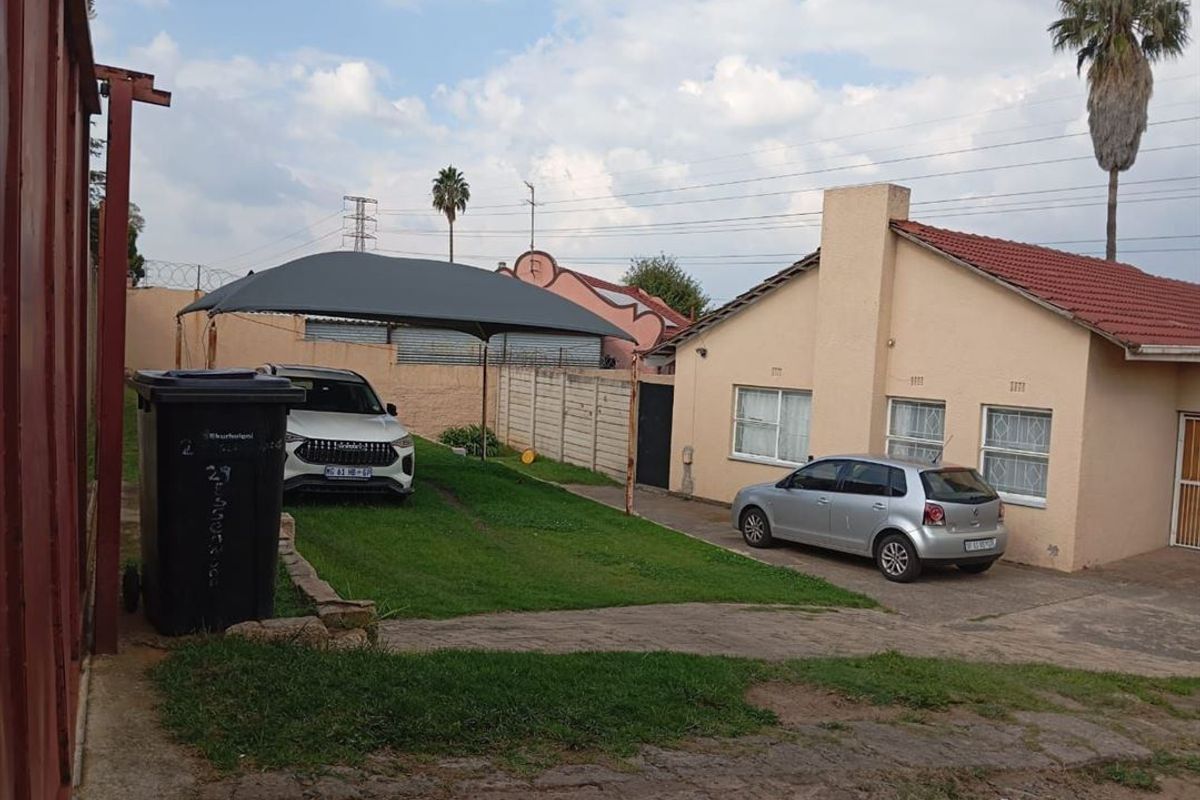 Rear exterior view of the property featuring a tiled roof, plastered walls, paved driveway, and a shade sail structure over the parking area.